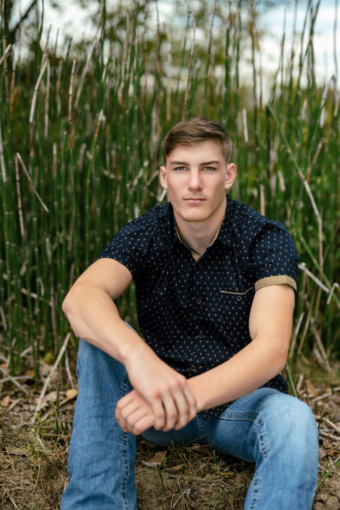 muscular High school senior guy sits in front of green bamboo