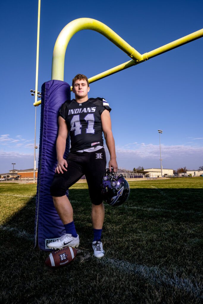 hallsville senior wearing football uniform leans on goal post