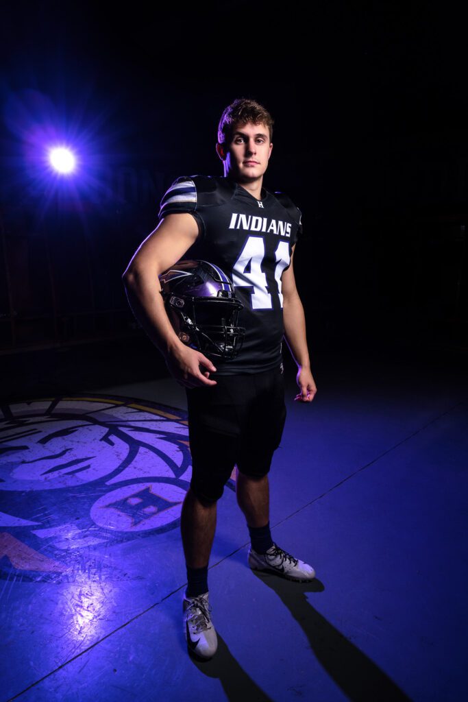 hallsville senior football player poses in locker room with helmet under arm.