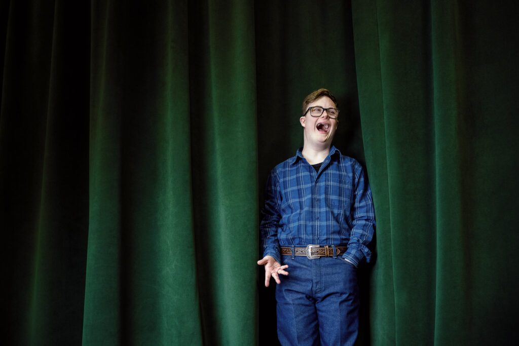 High school senior with Down Syndrome laughs while standing on stage by green curtain