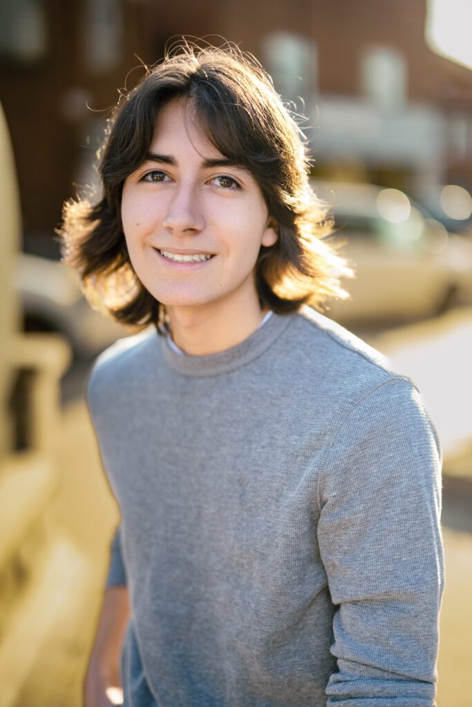 senior guy with long hair back lit by the sun wearing gray sweater