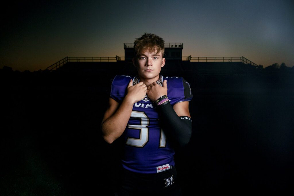 Hallsville high school senior football player wearing uniform standing in front of stadium at sunset