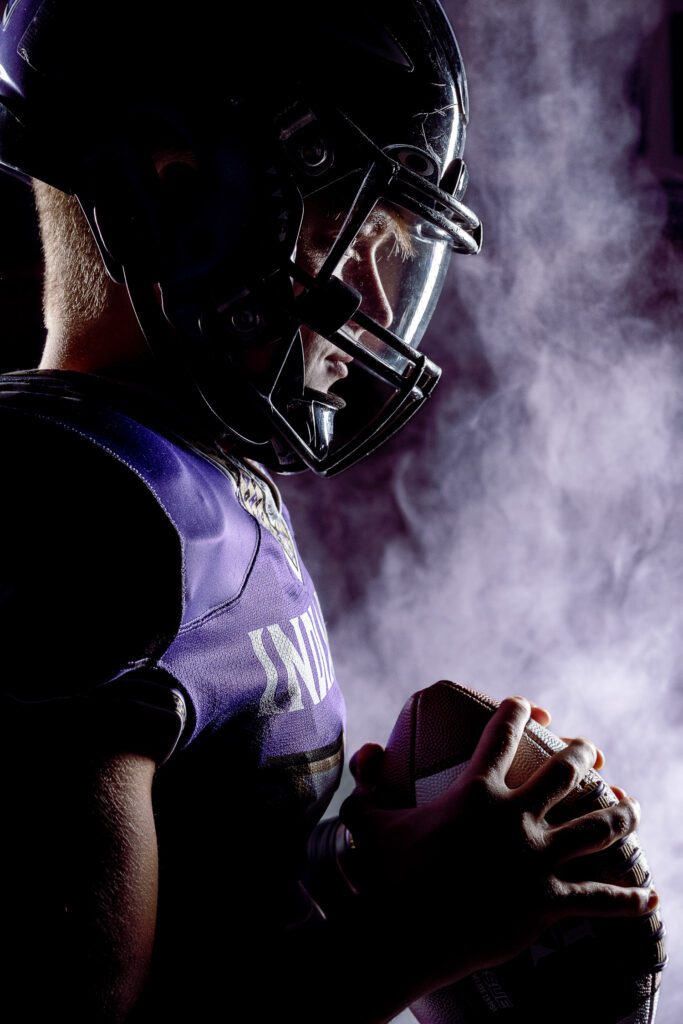 Hallsville senior football player holds football with light and smoke in background