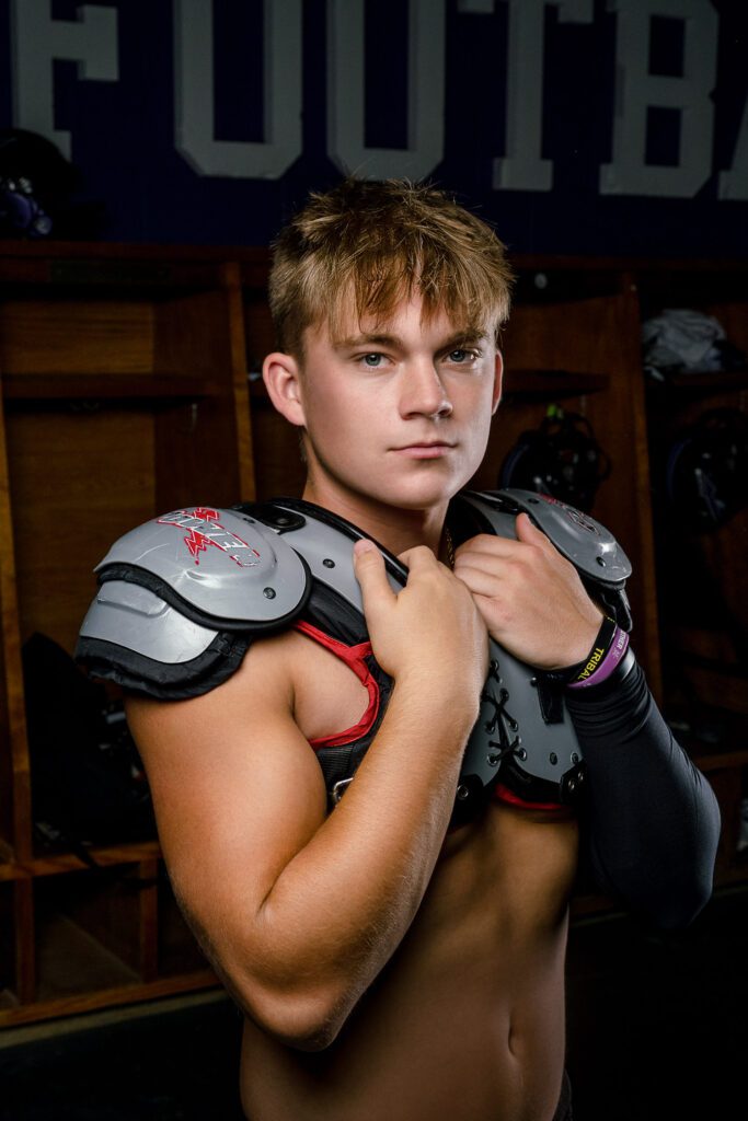 shirtless senior guy wearing football pads in Hallsville High School Locker Room