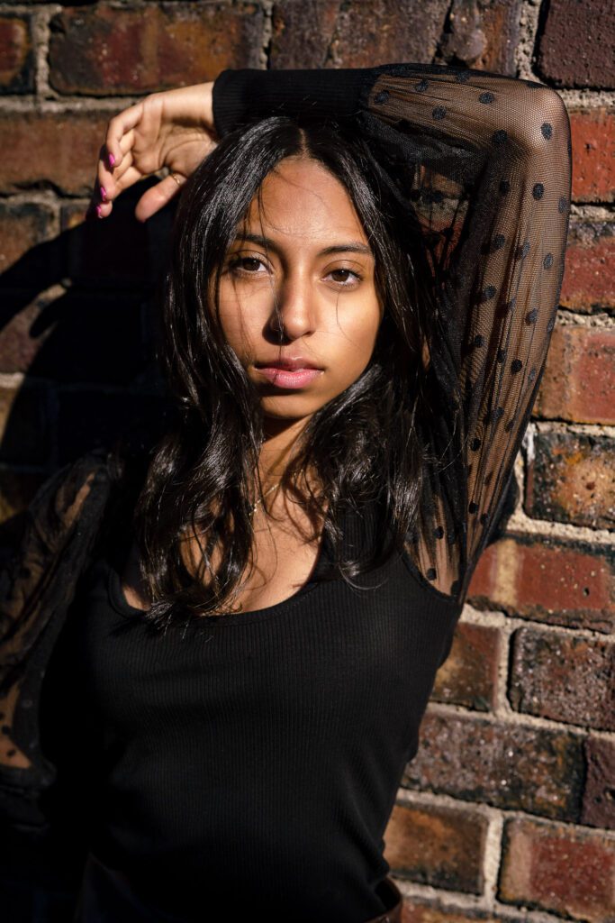 Senior girl wearing black top leans on brick wall in Columbia, Missouri.