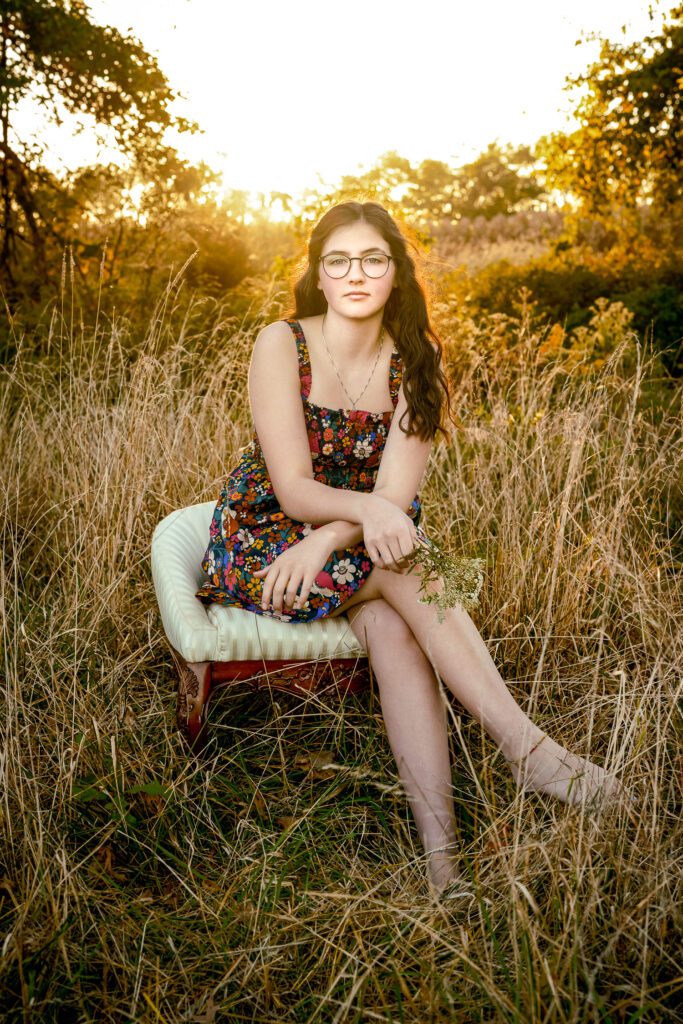 Senior girl sitting on white bench in field with warm sunlight