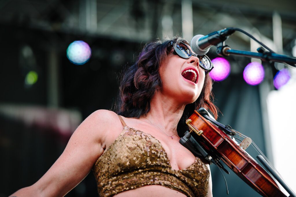 Amanda Shires wearing gold top while playing fiddle and singing.