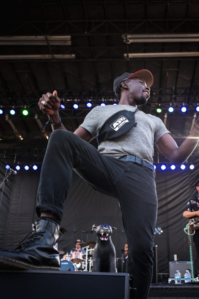 Black Pumas lead singer Eric Burton stands on speaker at the front of the stage.