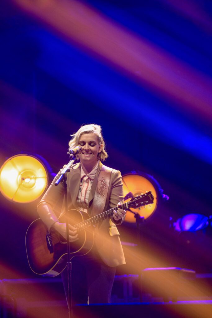 Brandi Carlile playing guitar under colorful stage lights.