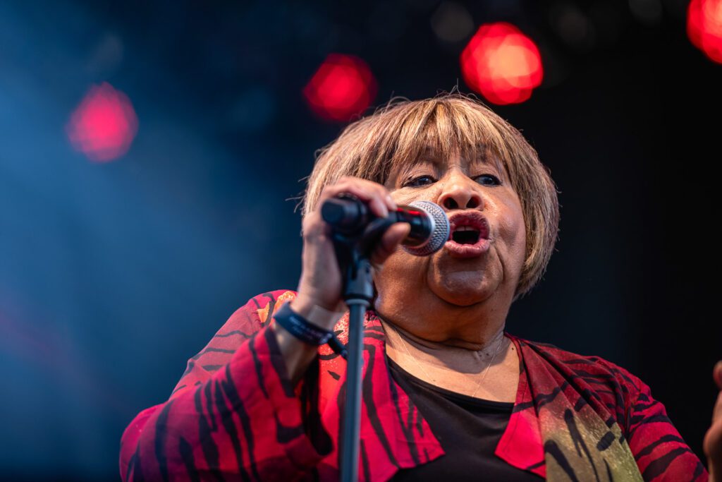 Mavis Staples sings into microphone wearing red top.