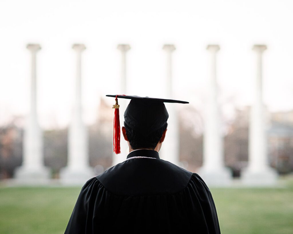 Senior wearing cap and gown looking at Mizzou Columns