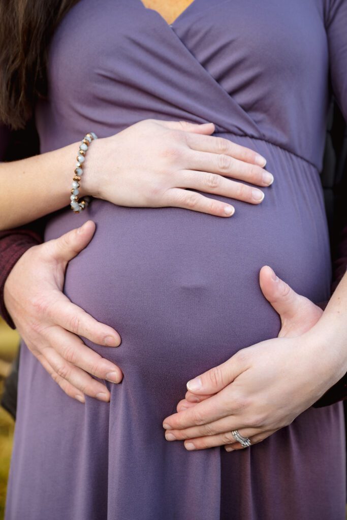 husband and wife have hands on pregnant belly during maternity session in columbia, missouri.
