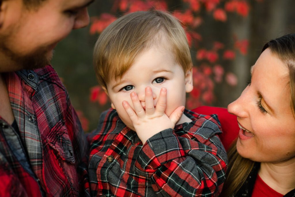 baby covering mouth with mom and dad in red plaid