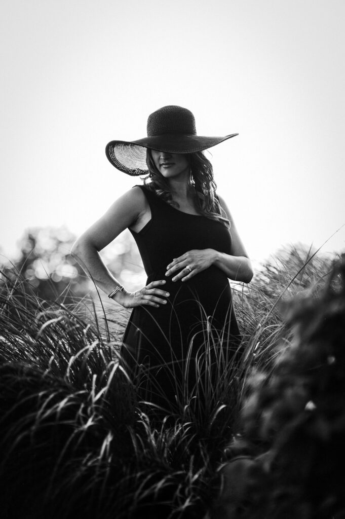 mother wearing big black hat holding pregnant belly in tall grass