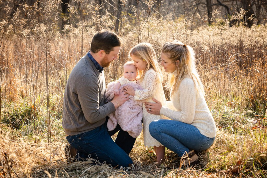 big sister kissing baby in field with parents Columbia, MO