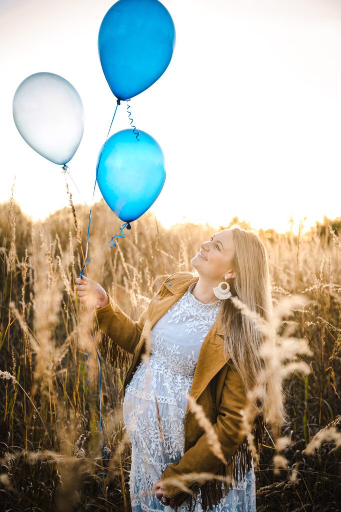 pregnant woman holding blue balloons in field