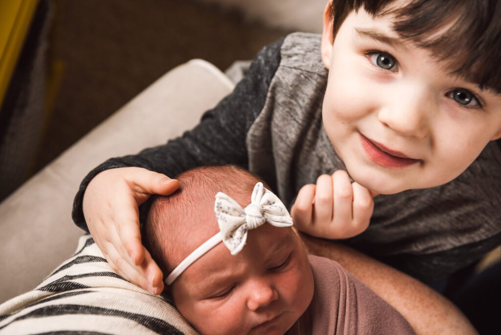 brother softly touches newborn sisters head while looking into camera