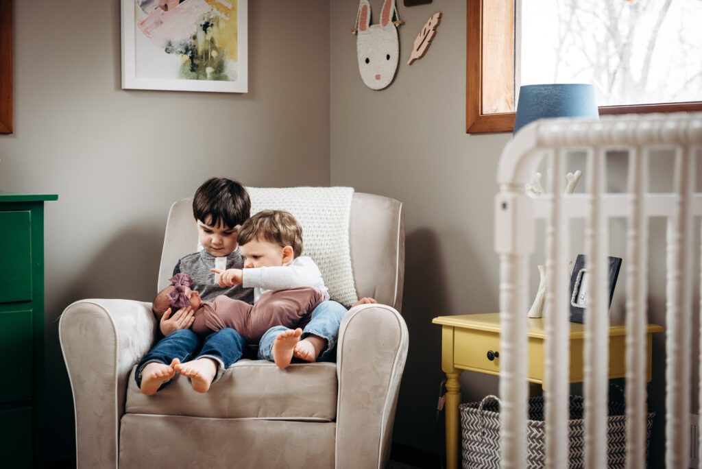 brothers holding baby sister in rocking chair in nursery
