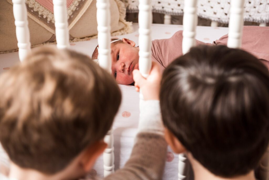brothers looking at newborn sister in crib through the bars