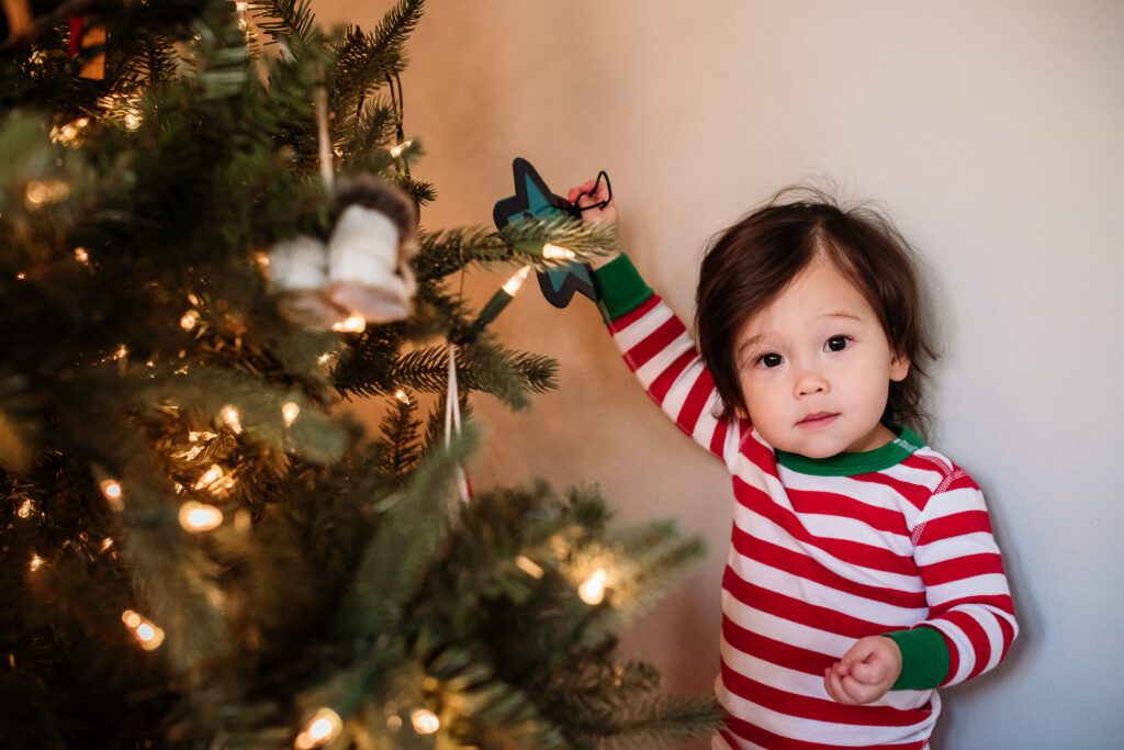 child holding ornament next to Christmas tree