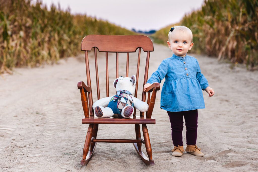 child with her teddy bear and chair in a cornfield