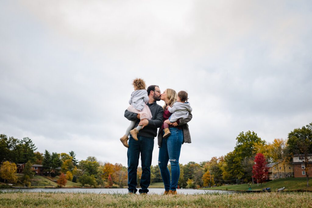 couple kissing holding kids near lake