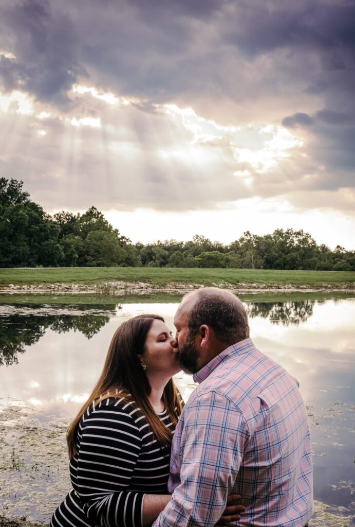 couple kissing in front of mirrored pond with clouds