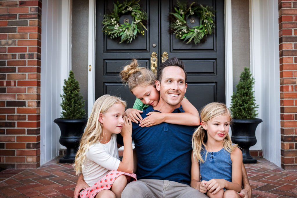 daughters hugging father on front porch of home in Columbia, MO