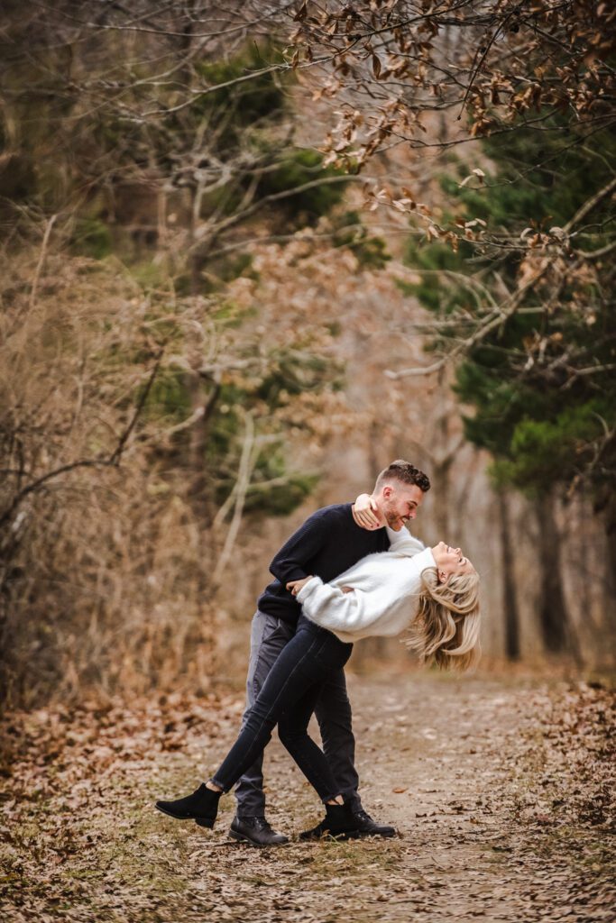 engaged man dipping fiance in wooded pathway