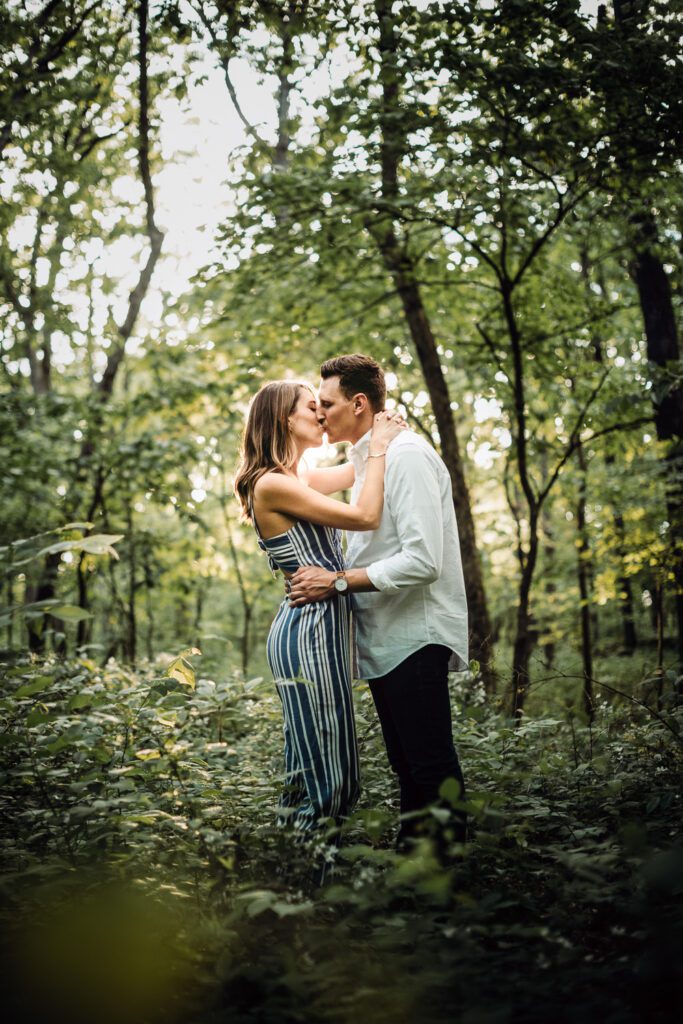 engaged couple kissing in the woods