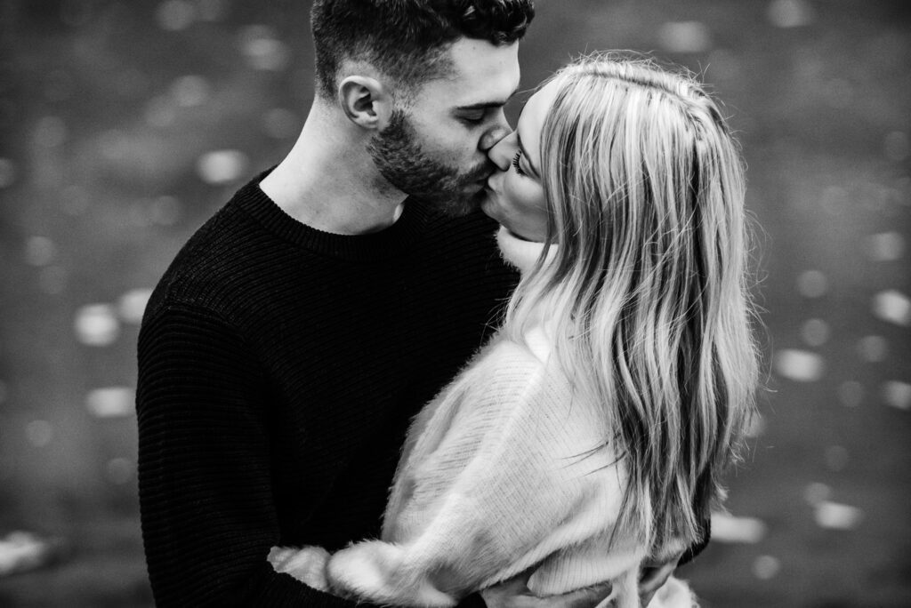 engaged couple kissing in front of water