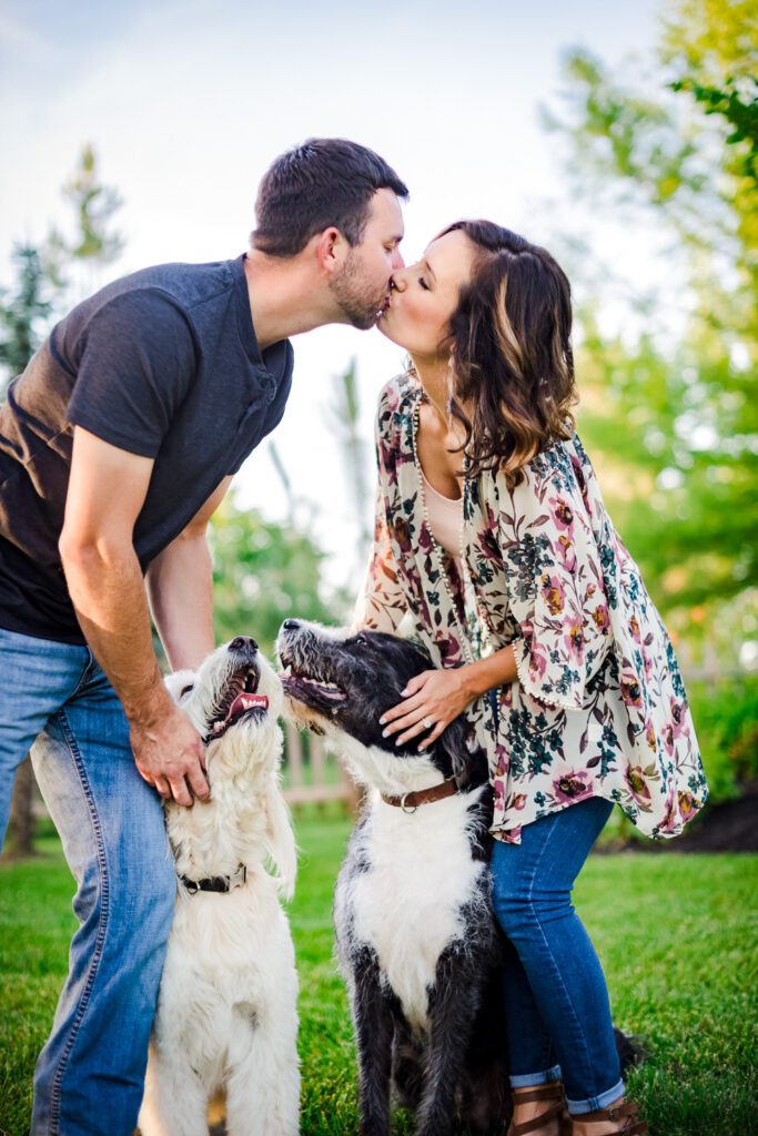 engaged couple kissing while holding two dogs