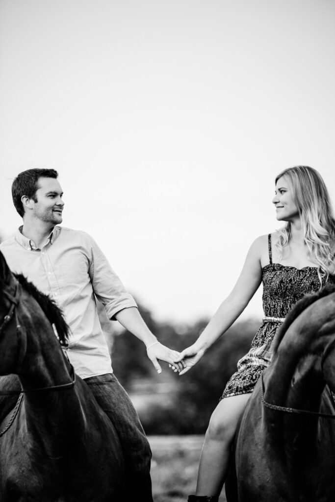 couple holding hands while riding horses