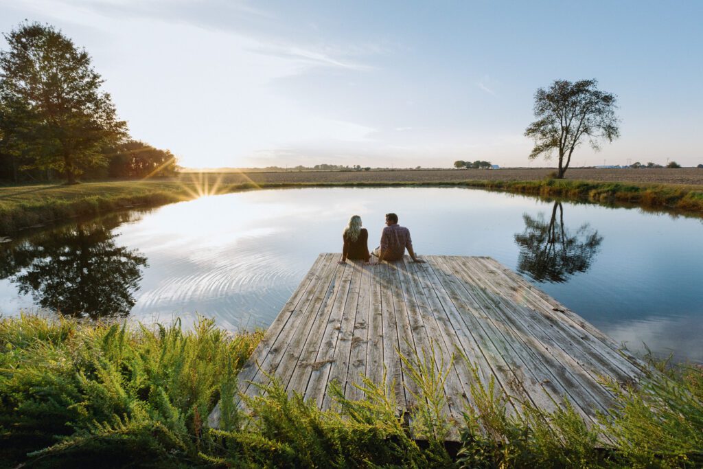 couple sitting on dock at sunset near pond