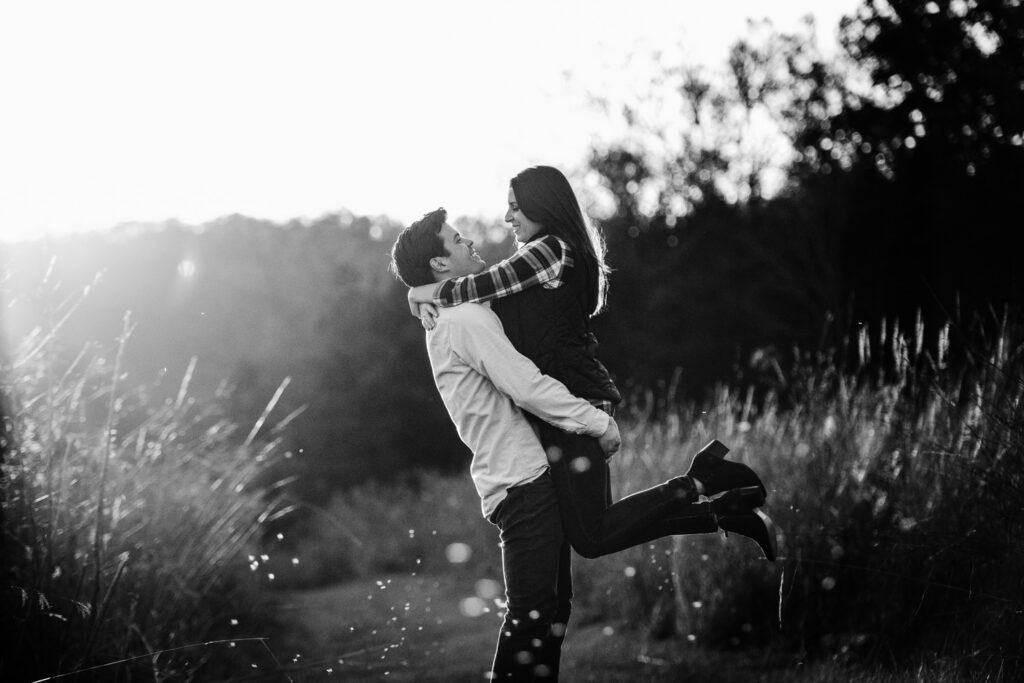 engaged couple holding fiance up in field of grassy field
