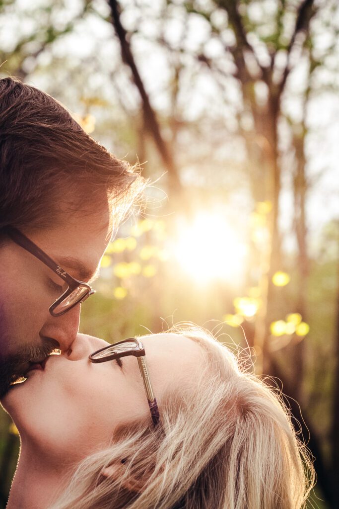 engaged couple wearing glasses kissing in the woods