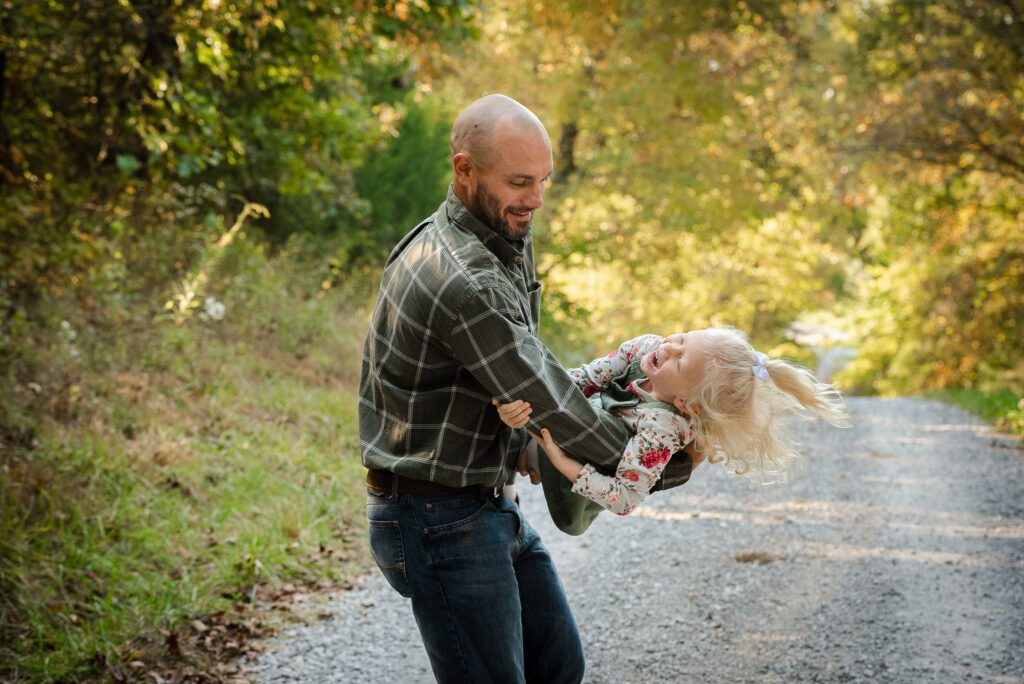 father tossing daughter around in woods gravel road in Columbia, MO
