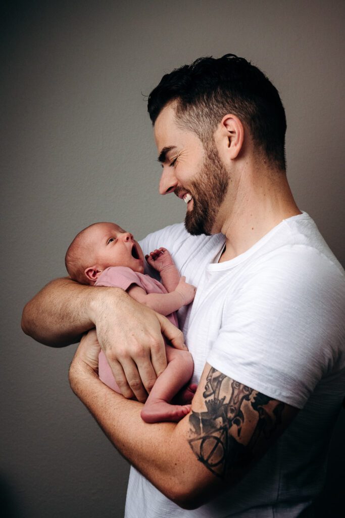 dad with tattoos holding yawning newborn baby in Columbia, MO