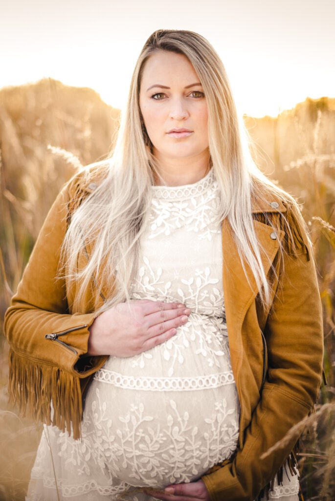 girl wearing fringe jacket in field holding pregnant belly