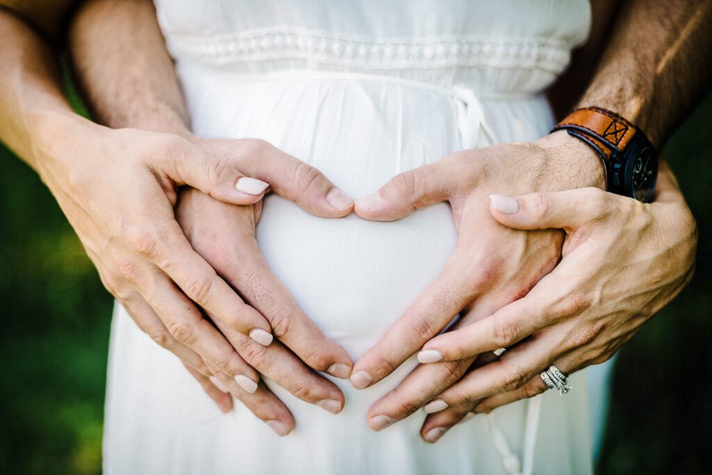 husband and wife making heart shape on pregnant belly with hands