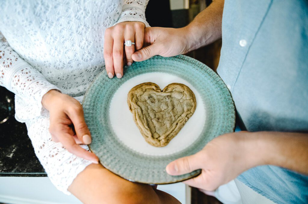 couple holding heart shaped cookie with engagement ring