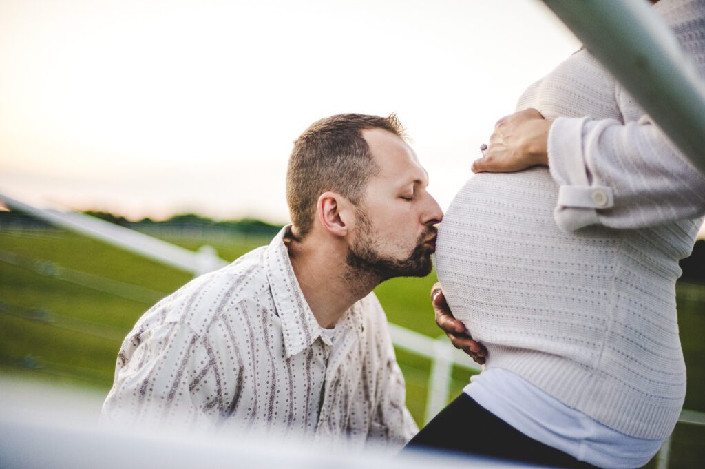 husband kissing wife's pregnant belly at Warm Springs Ranch, Boonville, Missouri