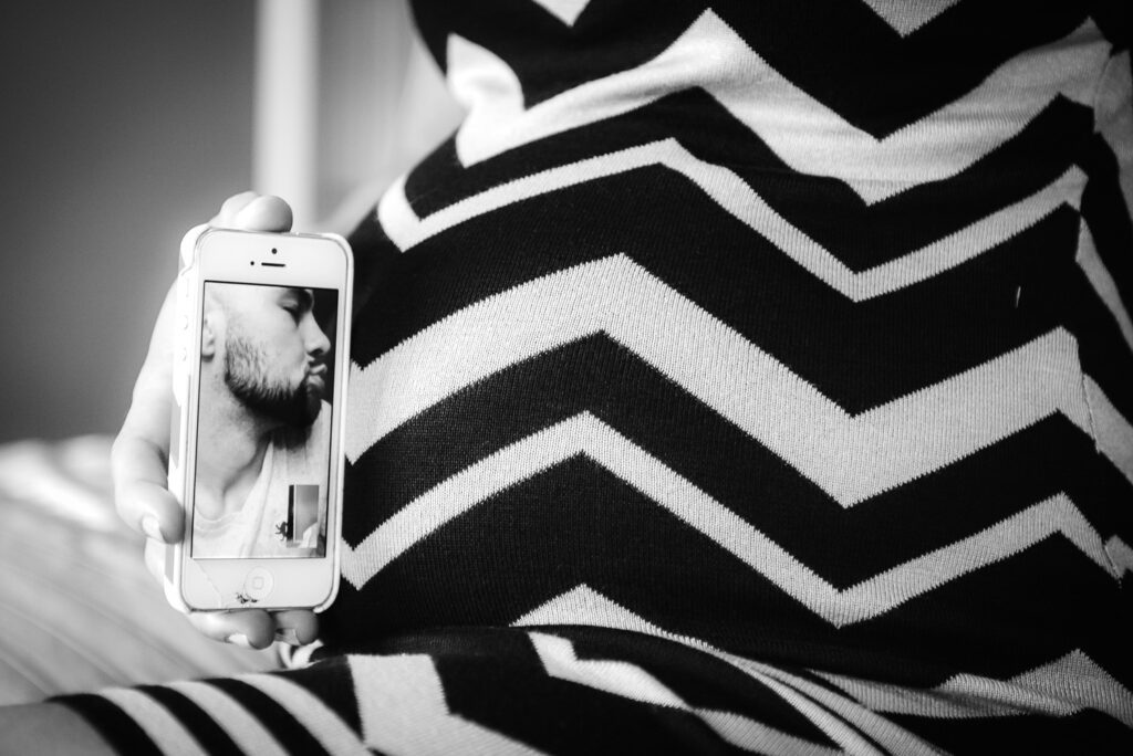 husband kissing pregnant belly through iphone overseas