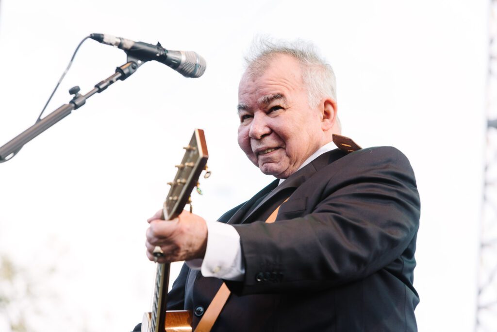 John Prine smiling while strumming guitar