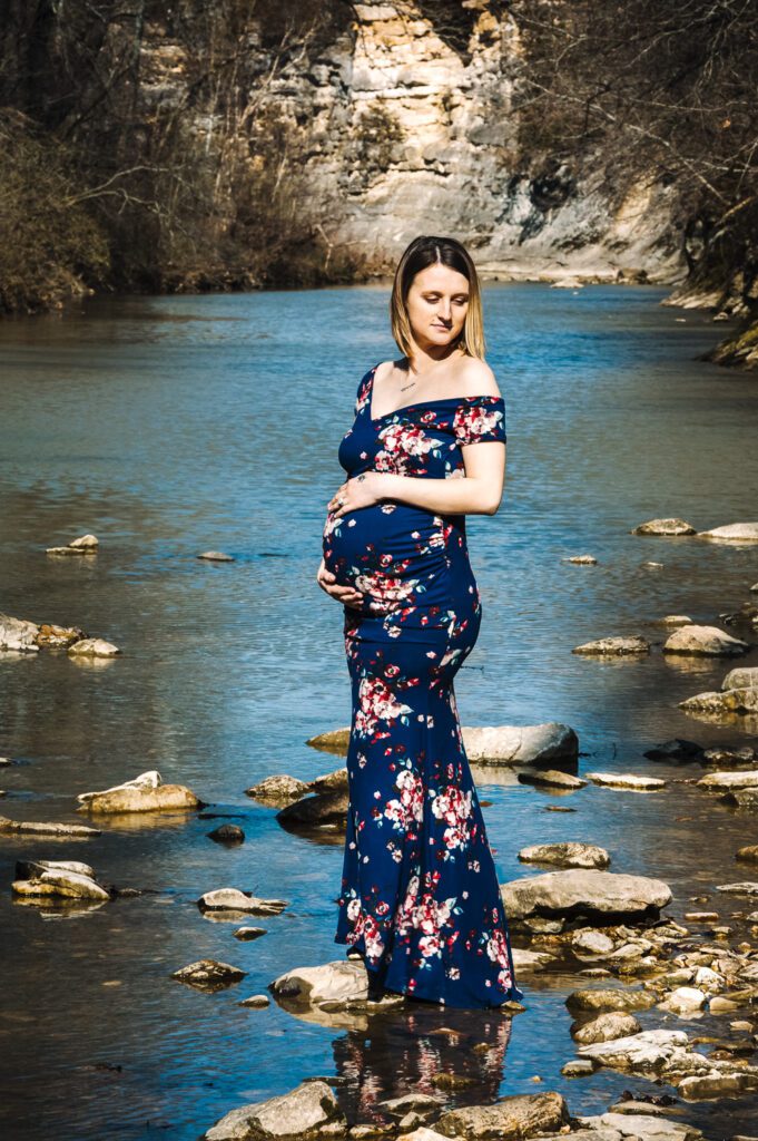 Pregnant woman in maternity evening gown on river rocks