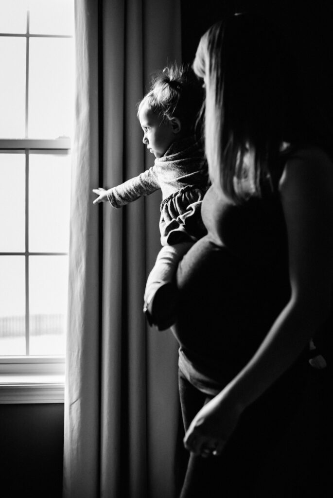 pregnant mother holding daughter in front of window