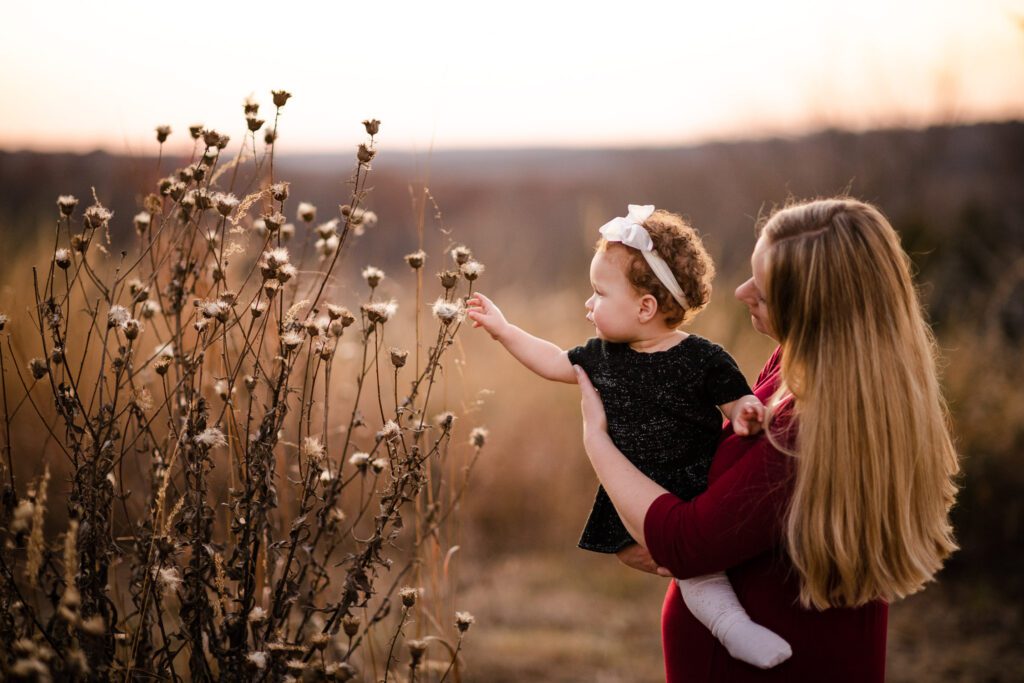 mother holding daughter grabbing flowers in field Columbia, MO