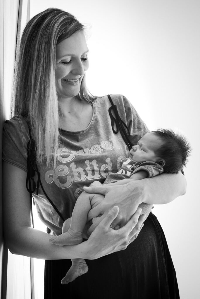 mother holding newborn while leaning on doorway at home in Columbia, MO