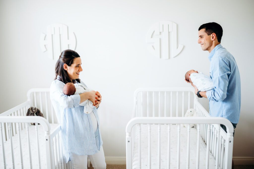 new mom and dad smiling by cribs with twins and monograms on wall in nursery