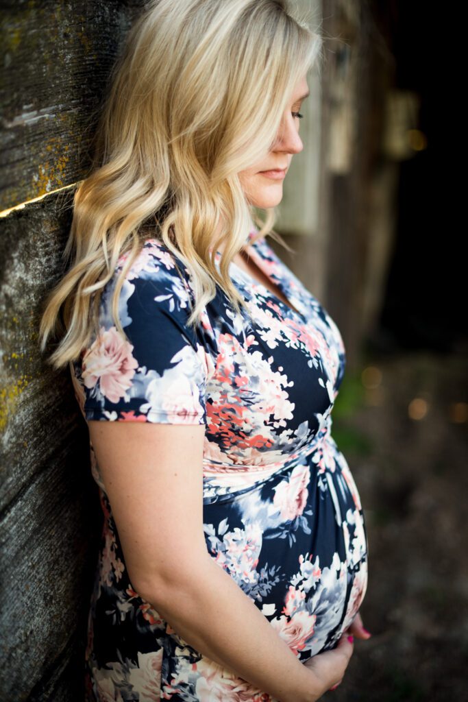 pregnant mother holding belly against barn